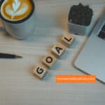 Motivational workspace featuring coffee, laptop, and "GOAL" blocks for positivity and productivity. setting goals
