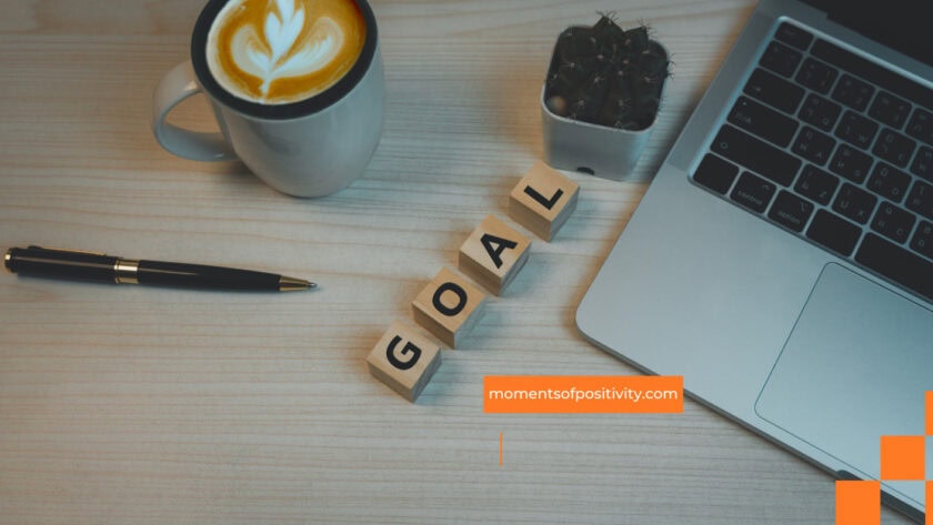 Motivational workspace featuring coffee, laptop, and "GOAL" blocks for positivity and productivity. setting goals